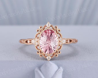 Könnte beinhalten: Ein Ring aus Roségold mit einem oval geschliffenen, hellrosa Mittelstein, der von einem dekorativen Filigranrahmen mit kleinen runden Akzentsteinen umgeben ist. Die Ringschiene hat ein gedrehtes Design und der Text PhoebeJewelryPalace ist sichtbar.