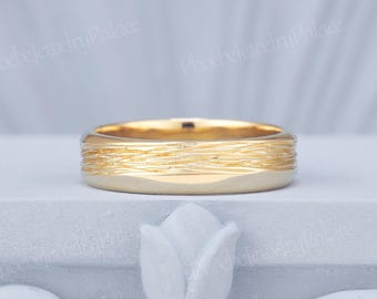 Op de afbeelding: Een gouden bandring met een getextureerd oppervlak met horizontale, onregelmatige, geëtste lijnen die rondom de gehele omtrek lopen. De ring heeft een gepolijste afwerking aan de randen en een matte, organisch ogende textuur in het midden.