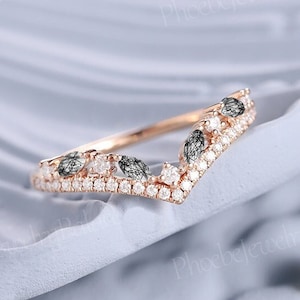 May include: A delicate rose gold wedding band with a V-shaped design. The band is adorned with small round diamonds and larger marquise-shaped black diamonds.