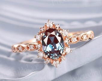 May include: A rose gold engagement ring with a large oval-shaped blue gemstone surrounded by a halo of smaller diamonds. The band is decorated with a delicate, intricate design.
