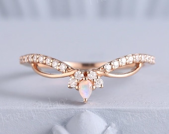 May include: A rose gold ring with a curved design, set with small clear stones and a central pear-shaped opal. The ring has a delicate, elegant appearance, perfect for a special occasion.