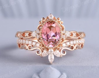 Könnte beinhalten: Ein Verlobungsring aus Roségold mit einem großen ovalen rosafarbenen Edelstein, der von kleineren klaren Edelsteinen umgeben ist. Der Ring hat ein zartes, verziertes Design mit filigranen Details.