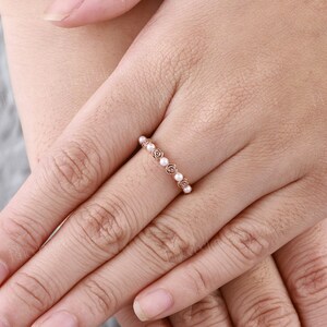 Pode incluir: Um delicado anel de banda de ouro rosa com uma fila de pequenas p&eacute;rolas brancas engastadas em motivos de rosas de ouro rosa.