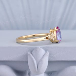 K&ouml;nnte beinhalten: Ein goldener Ring mit einem herzf&ouml;rmigen, lila und rosafarbenen Edelstein, umgeben von kleineren, klaren Edelsteinen.