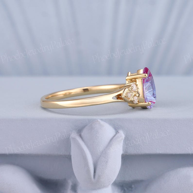 K&ouml;nnte beinhalten: Ein goldener Ring mit einem herzf&ouml;rmigen, lila und rosafarbenen Edelstein, umgeben von kleineren, klaren Edelsteinen.