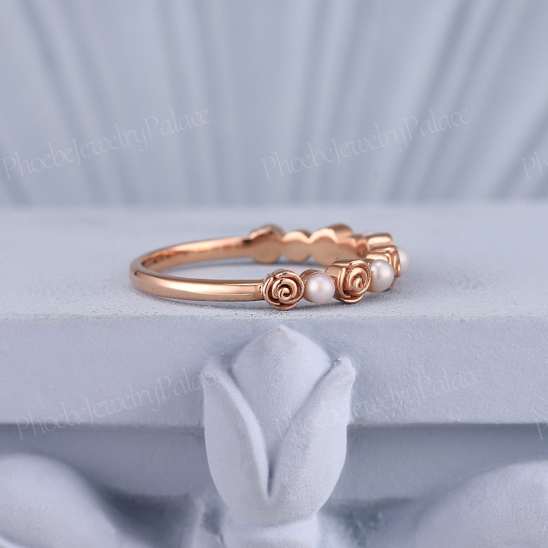 Pode incluir: Um delicado anel de banda de ouro rosa com uma fileira de pequenas p&eacute;rolas e detalhes de rosas.