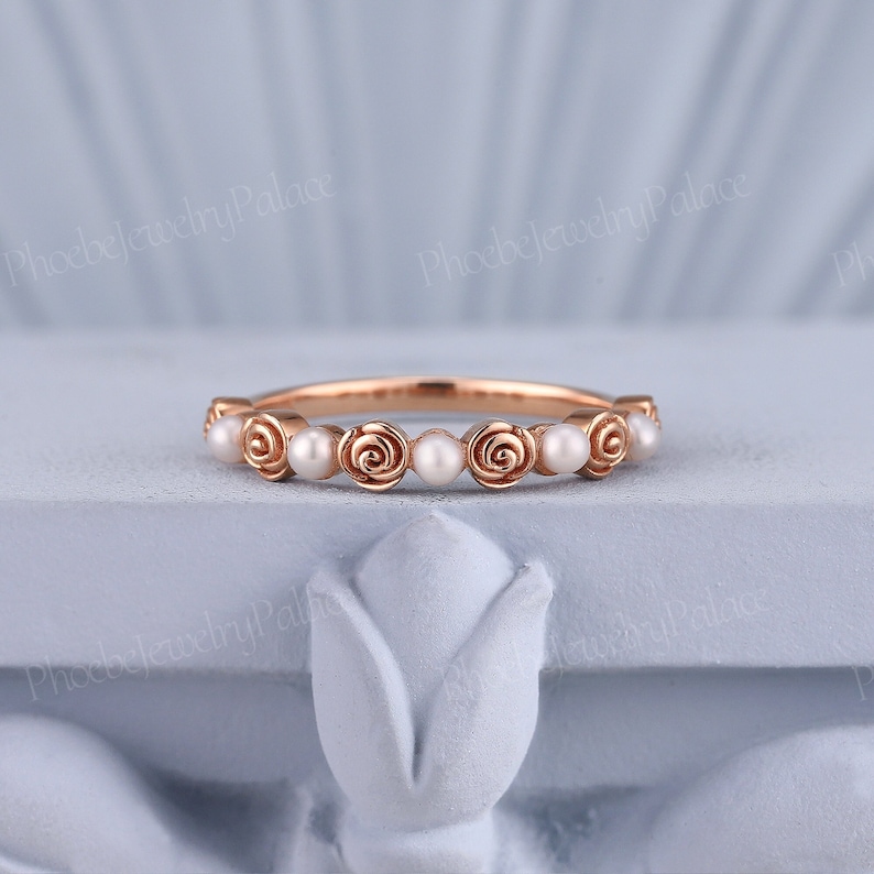 Pode incluir: Um delicado anel de banda de ouro rosa com uma fila de pequenas p&eacute;rolas brancas engastadas em motivos de rosas de ouro rosa.