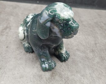 May include: A carved stone dog figurine in a seated pose. The sculpture is mainly dark green with white and light green marbling. The dog has detailed paws, ears, and a snout.