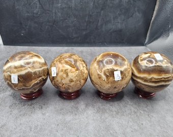 May include: Four decorative stone spheres with brown and cream-colored patterns, each resting on a small, round, dark red stand. Each sphere has a small white label with a number from 1 to 4.