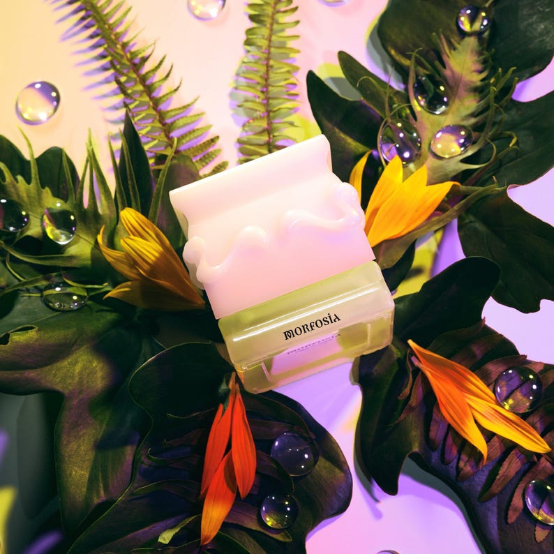 May include: A white and green product with the text "MORFOSIA" is surrounded by green leaves, yellow flowers, and water droplets. The product has a unique, wavy design on top. The background has a gradient of yellow and purple.