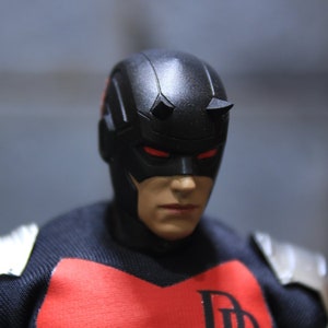 May include: A black and red superhero action figure with a black mask and red eyes. The figure is wearing a black suit with a red chest emblem.