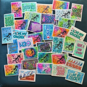 May include: A collection of colorful watercolor art cards with various phrases and illustrations. The cards feature phrases like "SATISFIED," "I LOVE MY CHICKEN," and "HAVE A GOOD SHOW." Each card has a unique design with vibrant colors and whimsical figures.