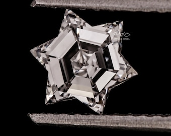 May include: A clear, faceted, star-shaped diamond held by tweezers. The diamond has a complex, geometric design with multiple facets.