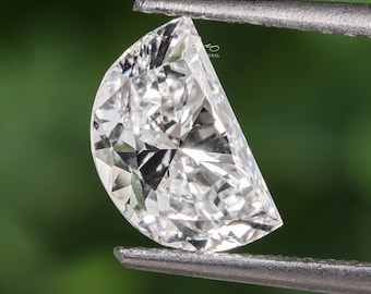 May include: A clear, round, half-moon shaped diamond gemstone held by tweezers against a green background.