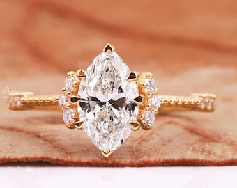 Puede incluir: Un anillo de compromiso de oro con un gran diamante de forma marquesa rodeado de diamantes más pequeños. El anillo tiene una banda delicada y adornada.