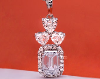 May include: A silver necklace with a pendant featuring a large, rectangular, clear emerald-cut gemstone surrounded by smaller clear gemstones. Three smaller heart-shaped gemstones are attached above the larger gemstone.