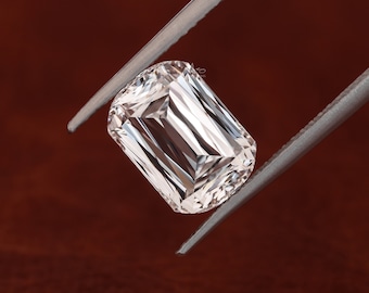 May include: A clear, rectangular, emerald-cut diamond gemstone held by silver tweezers against a brown background.