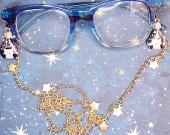 May include: Blue-framed glasses with a gold chain featuring star-shaped charms. The chain is attached to the glasses with small lightbulb-shaped charms.