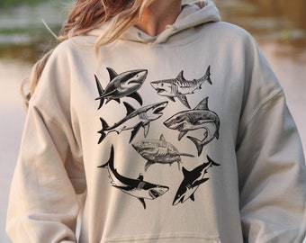 Op de afbeelding: Een beige hoodie met een grafische print van meerdere zwarte en witte haaien silhouetten.