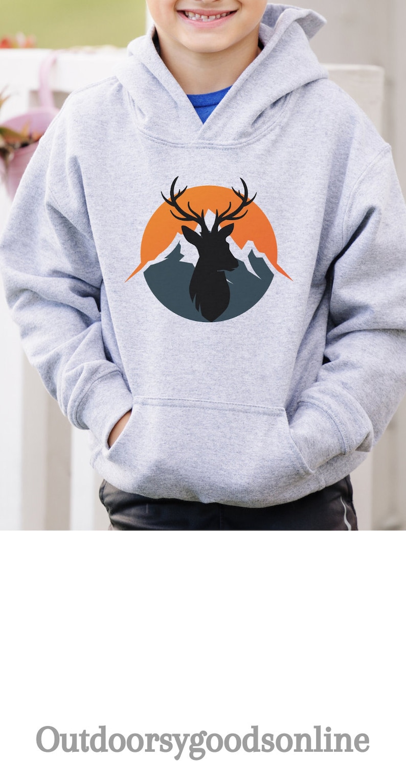 Puede incluir: Sudadera con capucha gris claro con bolsillo de canguro. Presenta un gr&aacute;fico circular de una silueta de ciervo con cuernos, sobre un fondo de monta&ntilde;as naranjas y azules. El texto "Outdoorsygoods online" est&aacute; en la parte inferior.