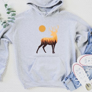 May include: A gray hooded sweatshirt with a graphic of a deer silhouette with a forest inside. The deer is standing in front of a yellow sun.