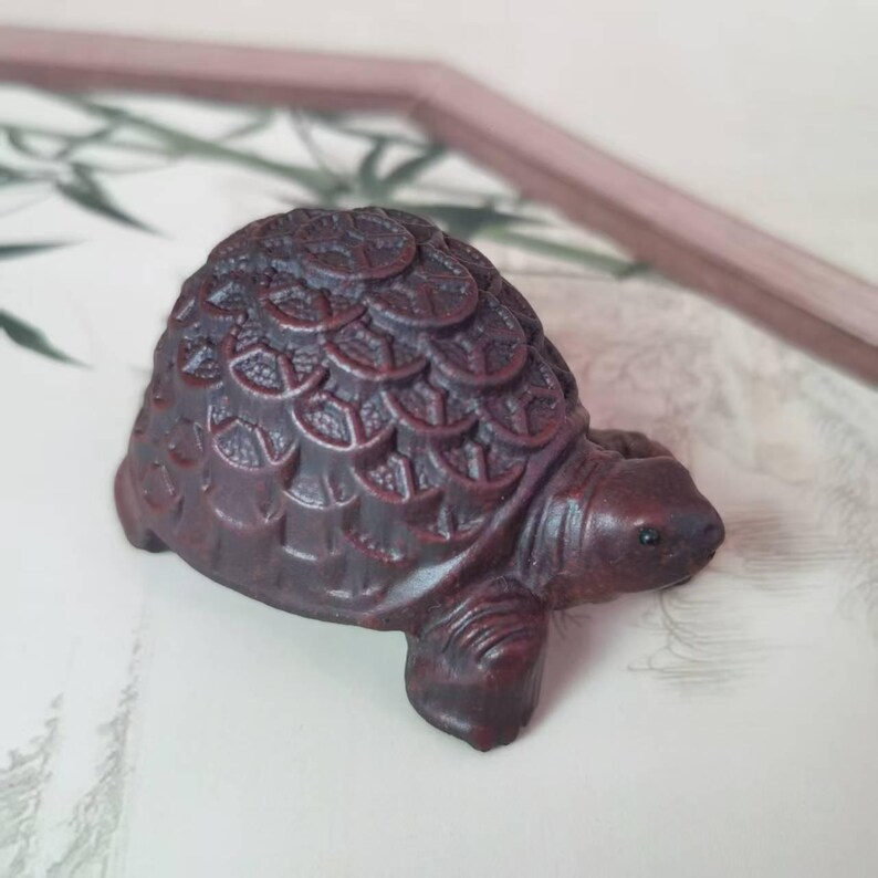 May include: A small, dark brown turtle figurine with detailed shell patterns. The figurine has a smooth, rounded body and a detailed head and legs. The turtle is made of a solid material and is likely a decorative item.