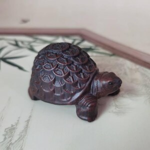 May include: A detailed wooden turtle figurine, carved with intricate patterns on its shell. The dark brown turtle has a smooth body and is set against a neutral background. The miniature sculpture showcases fine craftsmanship and detail, a charming decorative item.