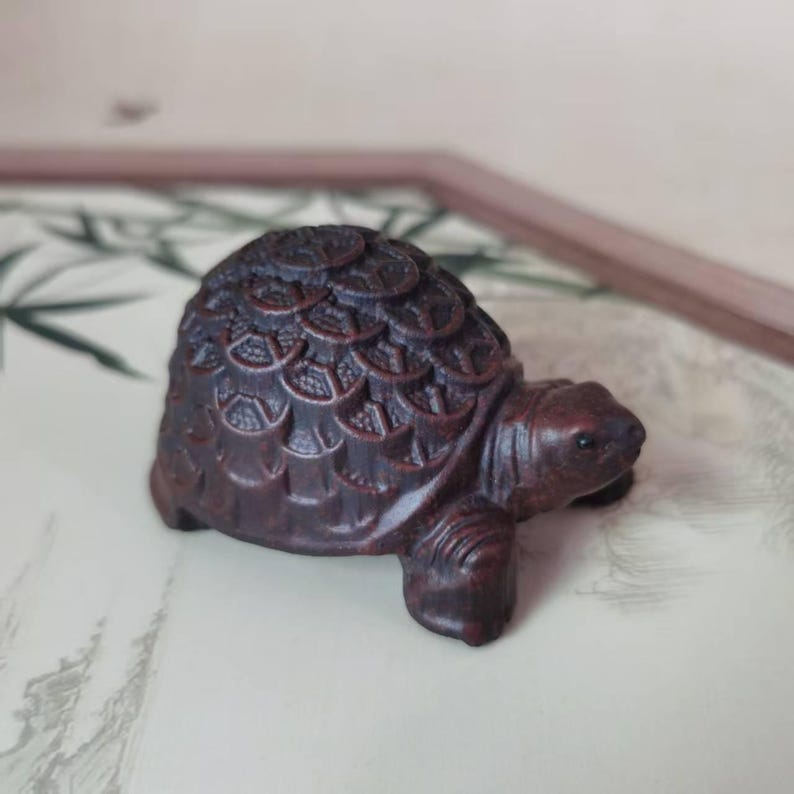 May include: A detailed wooden turtle figurine, carved with intricate patterns on its shell. The dark brown turtle has a smooth body and is set against a neutral background. The miniature sculpture showcases fine craftsmanship and detail, a charming decorative item.