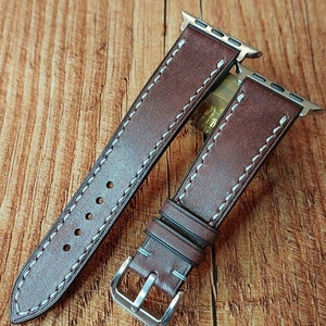 Pode incluir: Duas pulseiras de relógio de couro marrom com costuras brancas. As pulseiras são projetadas para Apple Watches e têm uma fivela prateada.
