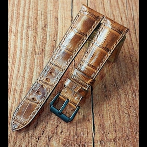 May include: A brown leather watch strap with a black buckle. The strap has a crocodile pattern.