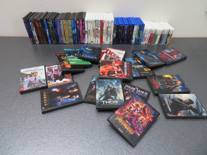 Peut inclure: Une collection de mini-DVD et Blu-ray de films. L'image pr&eacute;sente des piles de bo&icirc;tiers de diff&eacute;rentes couleurs, avec plusieurs couvertures de films individuelles &eacute;parpill&eacute;es devant. Les titres incluent "Avatar", "Thor" et "The Avengers".