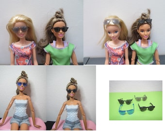 May include: Four dolls wearing sunglasses, with different hair colors and outfits. The sunglasses are black, gray, and blue. The dolls are wearing tops in various colors, including green, orange, and white, paired with denim shorts.