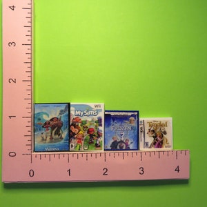 Peut inclure: Miniatures de jeux vid&eacute;o pour Wii et Nintendo DS, dont "Moana", "My Sims", "Frozen" et "Tangled". Les bo&icirc;tes sont dispos&eacute;es en rang&eacute;e, avec une r&egrave;gle rose en arri&egrave;re-plan. Les bo&icirc;tes mesurent environ 2.5 cm de hauteur.