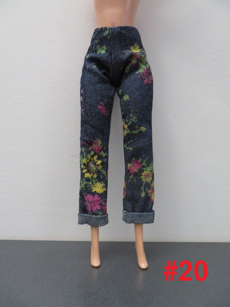 May include: Dark wash denim pants with a floral pattern in pink, yellow, and green. The pants have a straight leg cut and cuffed hems. The number "#20" is printed in red on the bottom right.