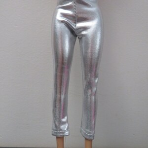 May include: Silver metallic pants with a textured surface. The pants are fitted and have a straight leg cut, with a seam down the front and back. The pants are designed for a doll.