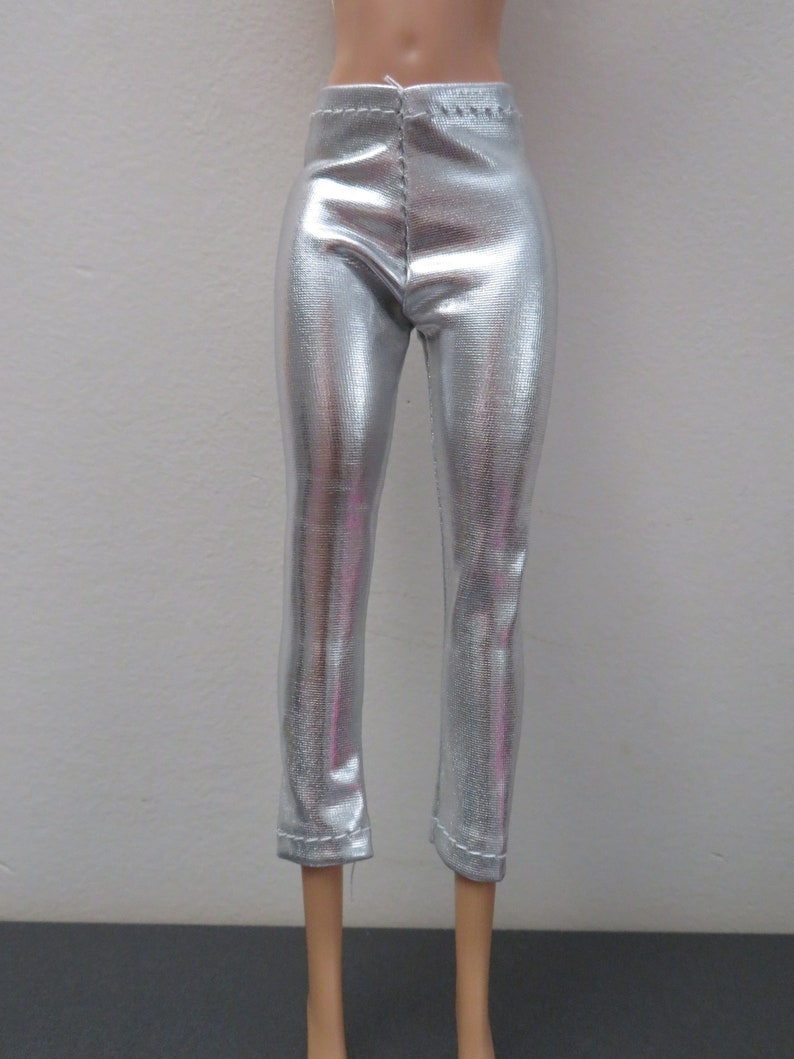 May include: Silver metallic pants with a textured surface. The pants are fitted and have a straight leg cut, with a seam down the front and back. The pants are designed for a doll.