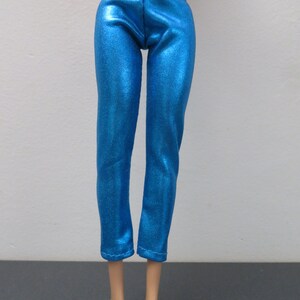 May include: Bright blue doll pants with a metallic sheen. The pants are a slim fit with a high waist and cropped length. The fabric has a subtle texture, reflecting light. The doll pants are designed for a fashion doll.
