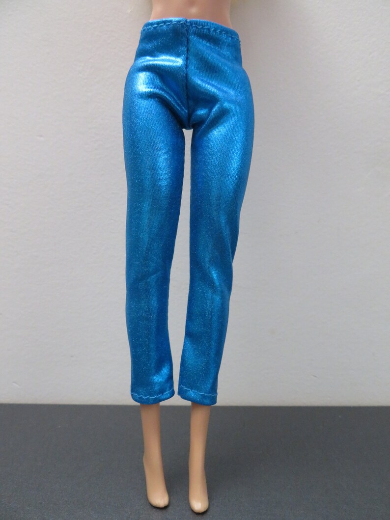 May include: Bright blue doll pants with a metallic sheen. The pants are a slim fit with a high waist and cropped length. The fabric has a subtle texture, reflecting light. The doll pants are designed for a fashion doll.