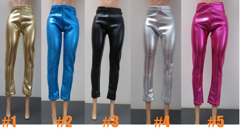 May include: Five pairs of doll-sized pants in various metallic colors: gold, blue, black, silver, and pink. Each pair has a shiny, smooth texture and a fitted design. The pants are displayed on doll legs.