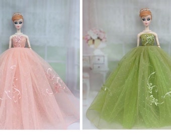 May include: Two dolls wearing elegant gowns. One doll is in a light pink dress with floral embroidery, and the other is in a green dress with similar embroidery. Both dresses have a full, flowing skirt.