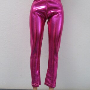 May include: Bright pink, metallic-finish pants. The pants have a high waist and a straight leg cut, with a slight flare at the ankle. The fabric has a textured appearance, reflecting light. The pants are designed for a doll.