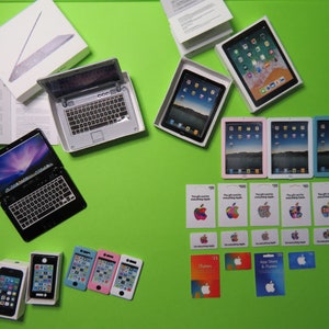 May include: An assortment of Apple products, including laptops, tablets, and iPhones, are displayed on a bright green surface. Gift cards with the Apple logo and iTunes cards are also present, suggesting a tech-themed gift set.