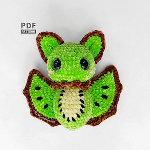Peut inclure: Une chauve-souris en crochet avec un corps vert vif, un ventre crème marqué de points noirs, de grands yeux sombres, des joues roses et des ailes et oreilles bordées de brun. Le texte PDF PATTERN et WysineCrochet est visible.