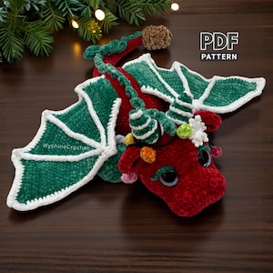 May include: A handmade red and green crochet dragon with white accents. The dragon has large green wings with white trim, and is decorated with colorful lights. The text "PDF PATTERN" is visible in the image.