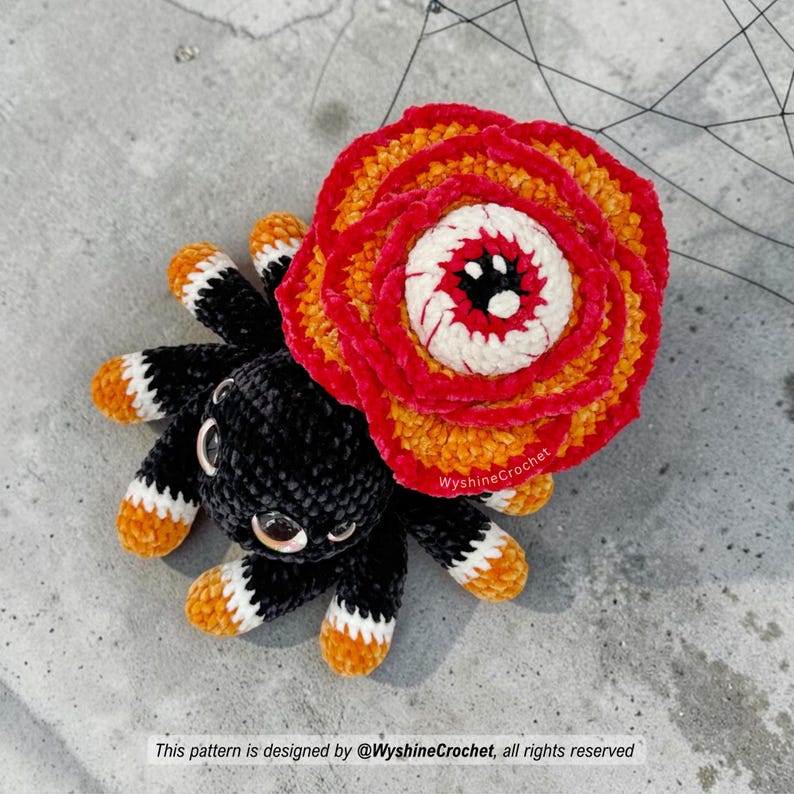 Rose-Eyed Spider amigurumi plushie with layered red and orange crochet petals, black chenille spider body, and creepy cute Halloween look