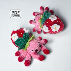 May include: Three crocheted strawberry octopus toys. Two are red with white flower accents and green leaves. The other is pink with red accents. The toys have black eyes and are on a white background. The words "PDF PATTERN" are in a white box in the upper left corner.