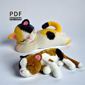 Könnte beinhalten: Zwei handgefertigte gehäkelte Katzenplüschtiere in Schlafposition. Die Katzen haben weißes, gelbes, schwarzes und braunes Fell mit rosa Akzenten an Ohren und Nase. Das Bild enthält den Text "PDF PATTERN".