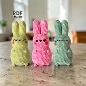 Op de afbeelding: Drie handgemaakte gehaakte konijnen in pastelkleuren: geel, roze en groen. Elk konijn heeft een lachend gezicht met roze wangen en knoopogen. De tekst "PDF PATTERN" staat in de linkerbovenhoek.