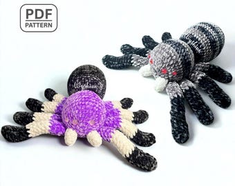 May include: Two plush crochet spiders. One is purple with cream and black legs, the other is gray and black. Both have a round body and eight legs. The spiders are handmade and have the text "PDF PATTERN" in the upper left corner.