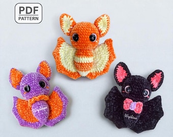 May include: Three handmade crochet bats in orange, purple, and black. The bats have large eyes and detailed wings. The orange bat has cream-colored wings, the purple bat has orange wings, and the black bat has pink accents. The image includes the text "PDF PATTERN".